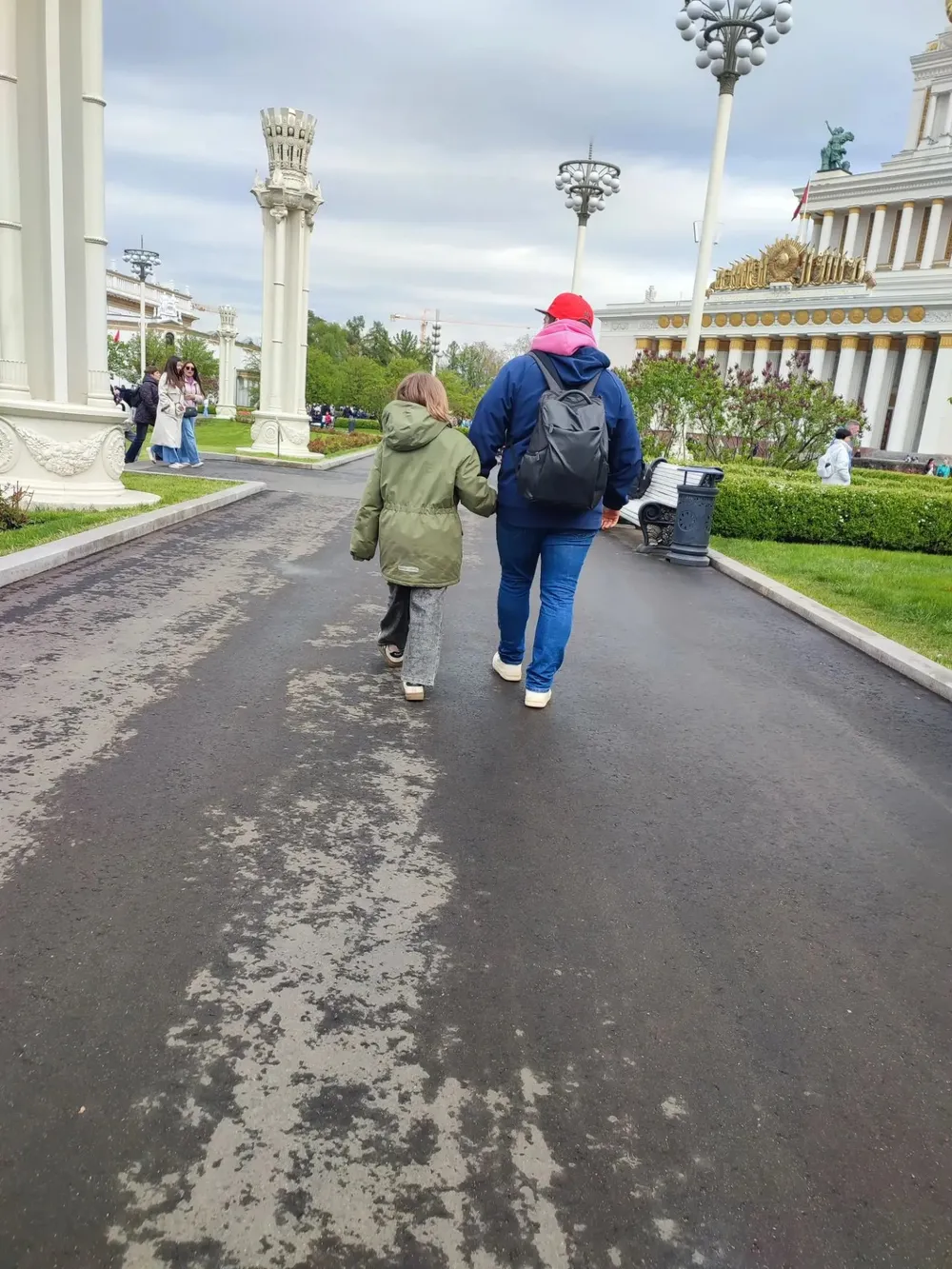 Кирилл с дочерью держатся за руки, вид со спины, идут по аллее